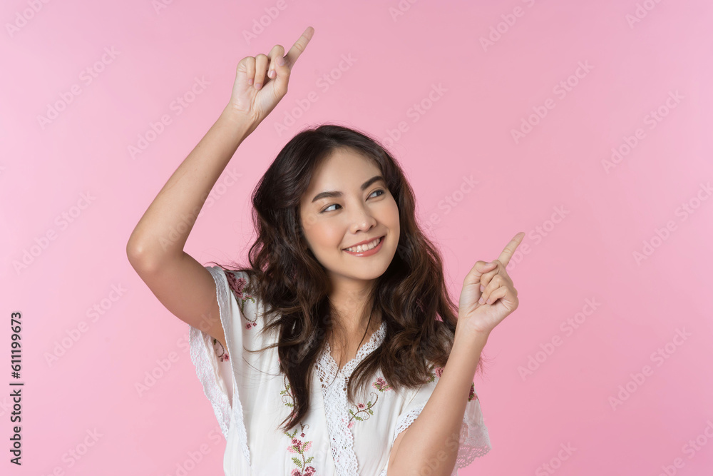 Young Asian woman pointing fingers up to empty space isolated pink color background