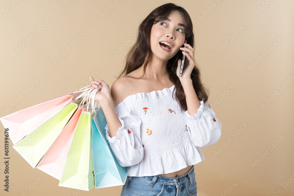 Young Asian woman usin shopping bag using phone on isolate brown background