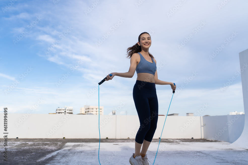 Young Asian woman with jump rope on rooftop. Fitness female doing skipping workout outdoors