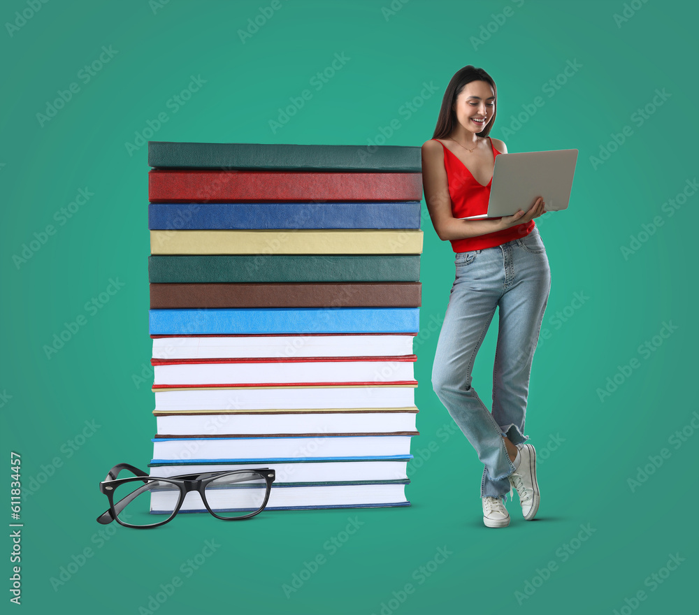 Beautiful young woman with laptop and stack of big books against green background