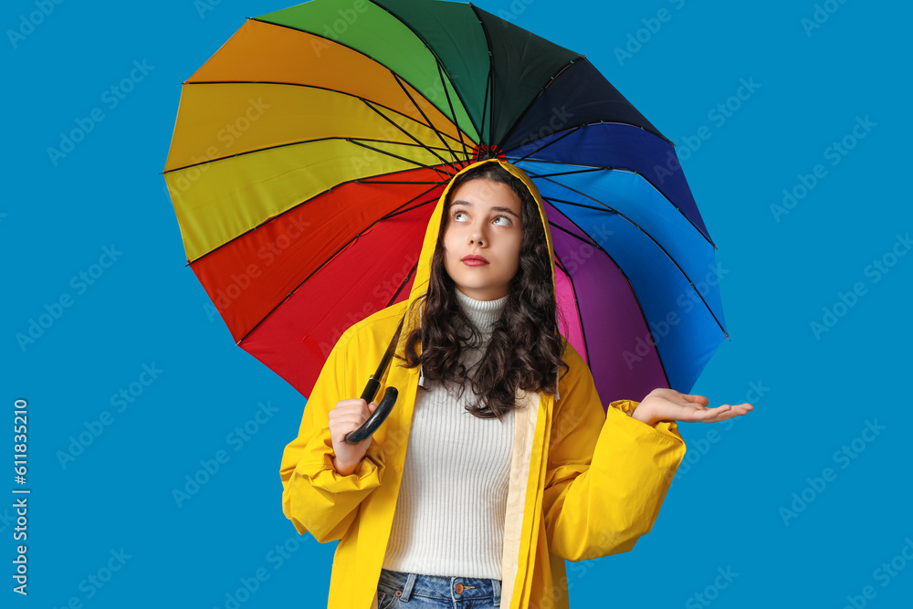 Teenage girl in raincoat with umbrella on blue background