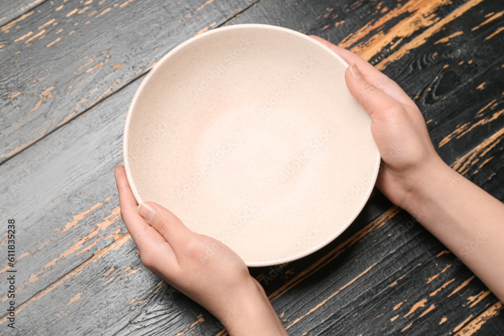 Female hands with empty plate on black wooden background