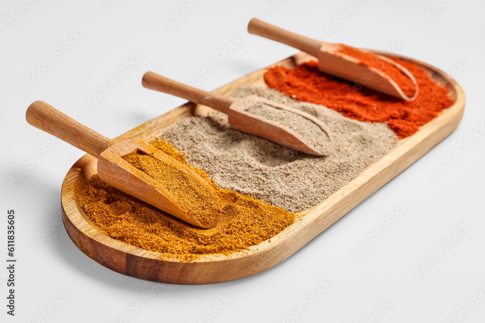 Wooden board with scoops of aromatic spices on light background