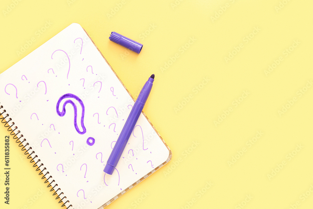 Notebook with drawn question marks and marker on yellow background