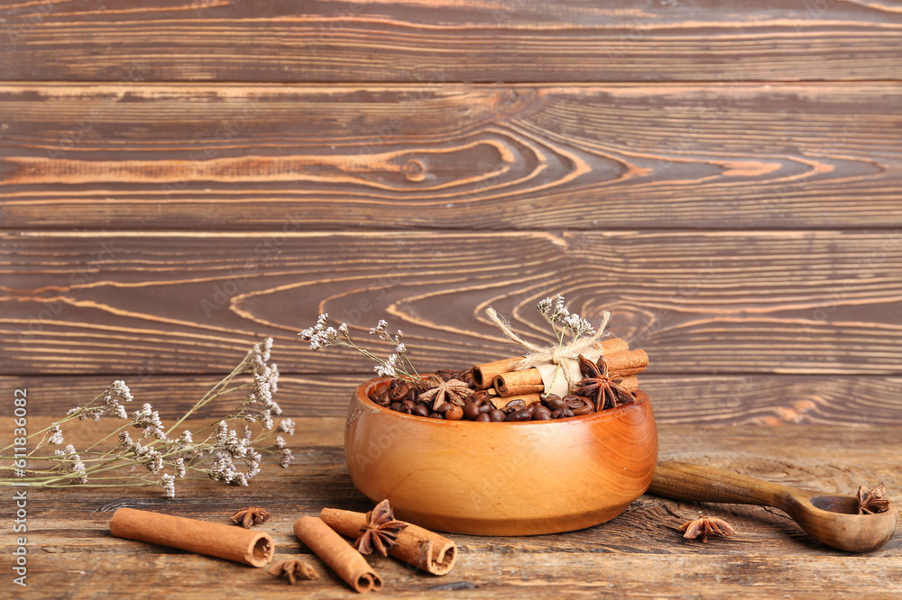 Bowl of coffee beans, cinnamon sticks and dried flowers on wooden background