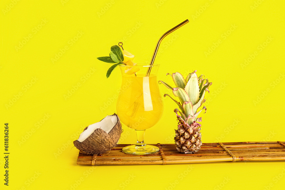 Glass of cocktail with baby pineapple and coconut on yellow background