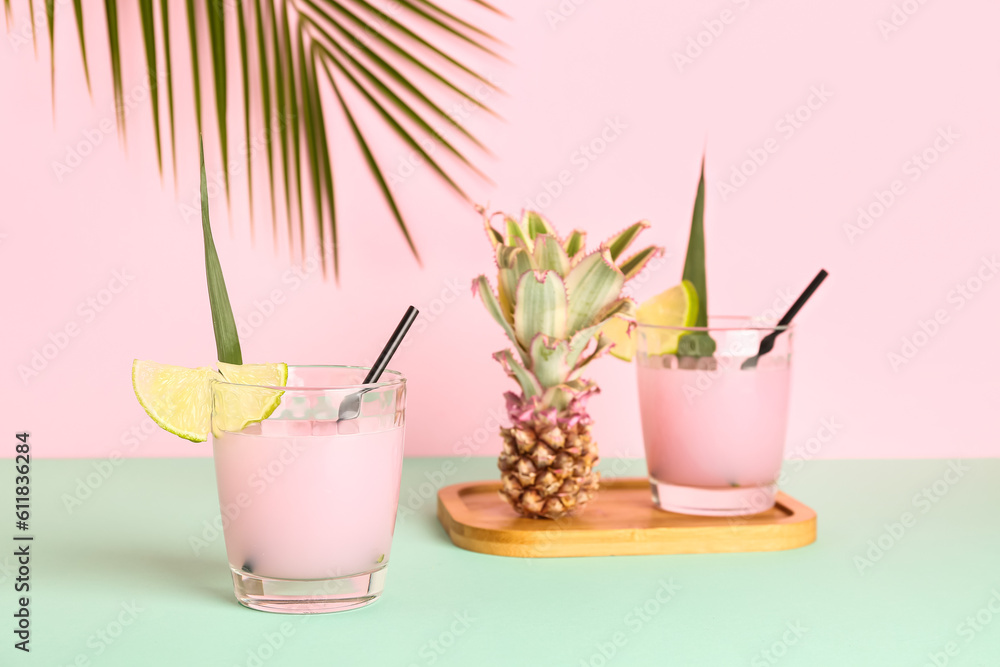 Glasses of cocktail with lime and baby pineapple on table near pink wall, closeup