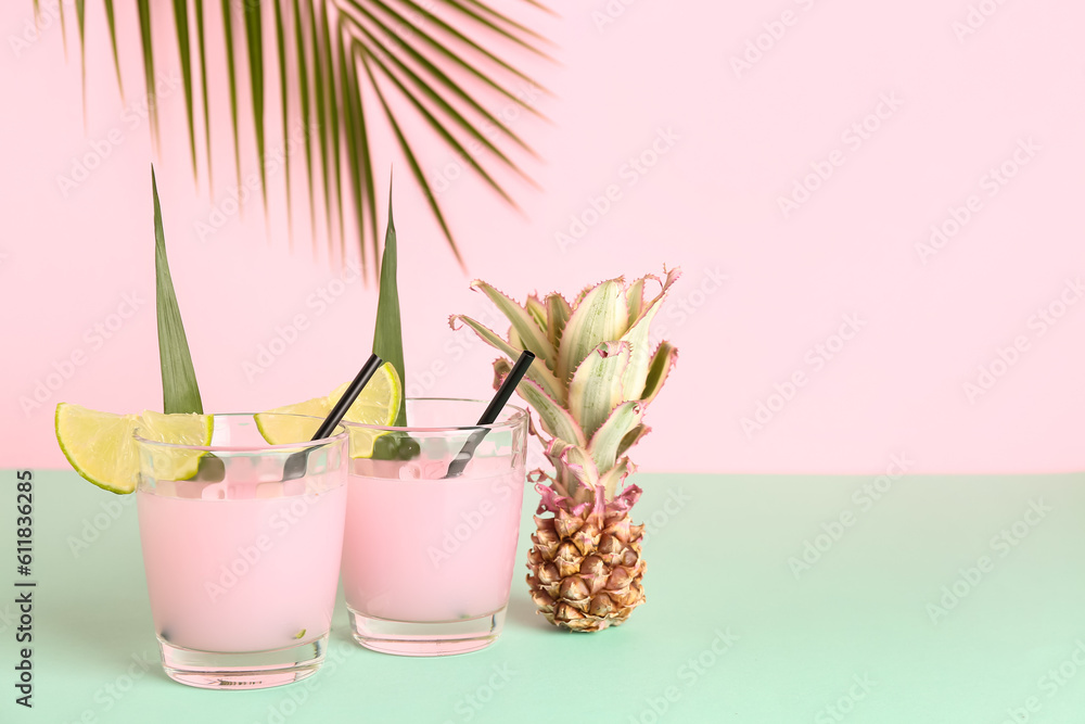 Glasses of cocktail with lime and baby pineapple on table near pink wall