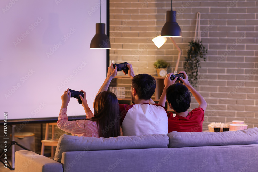 Father with his little children playing video game at home in evening, back view