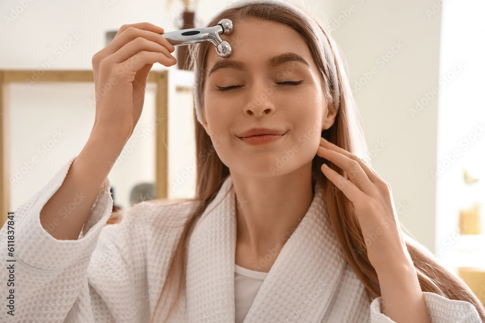 Young woman with facial massage tool in bathroom, closeup