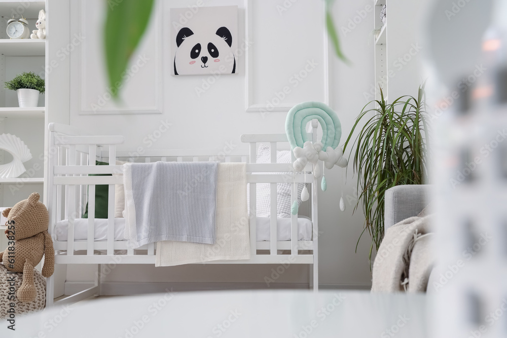 Stylish interior of childrens room in white tones with baby bed and shelving unit