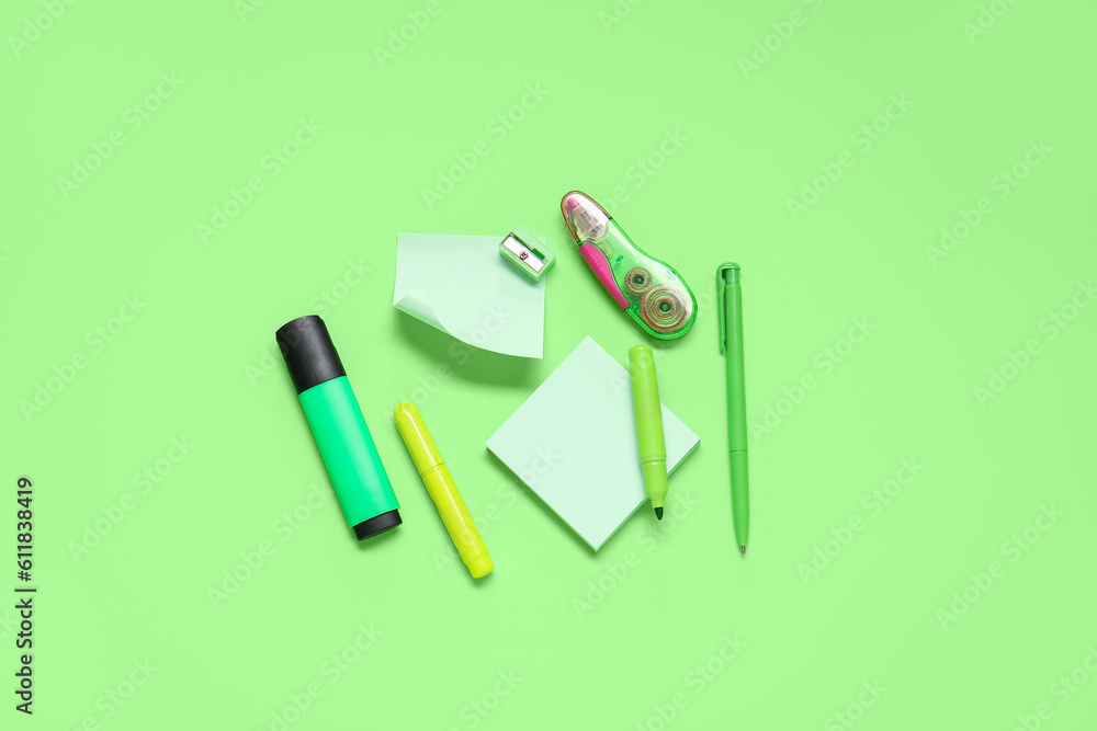 Sticky notes with different stationery supplies on green background