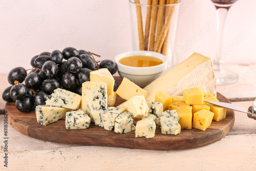 Wooden board with pieces of tasty cheese and grapes on table