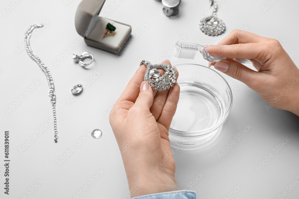 Woman cleaning beautiful jewelry with toothbrush on white background, closeup