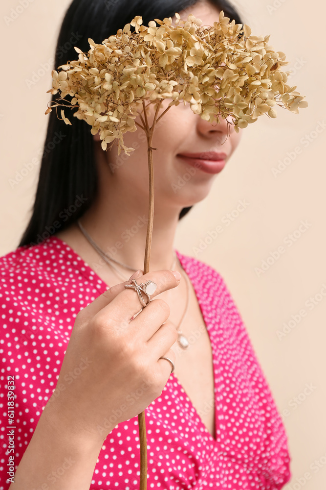 Beautiful young woman wearing elegant jewelry with flowers near beige wall