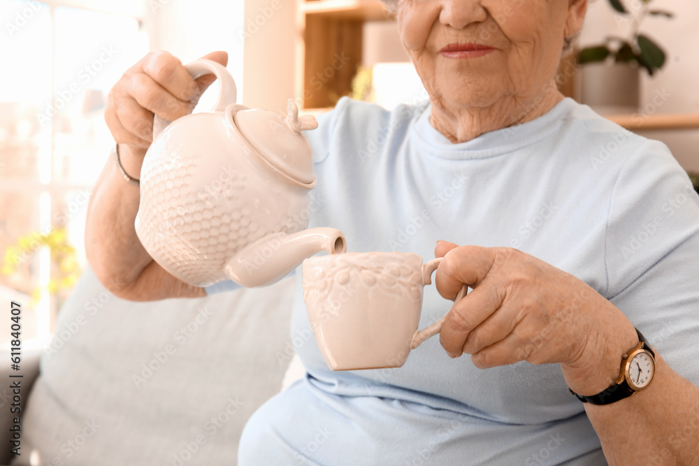 Senior woman pouring tea into cup at home, closeup