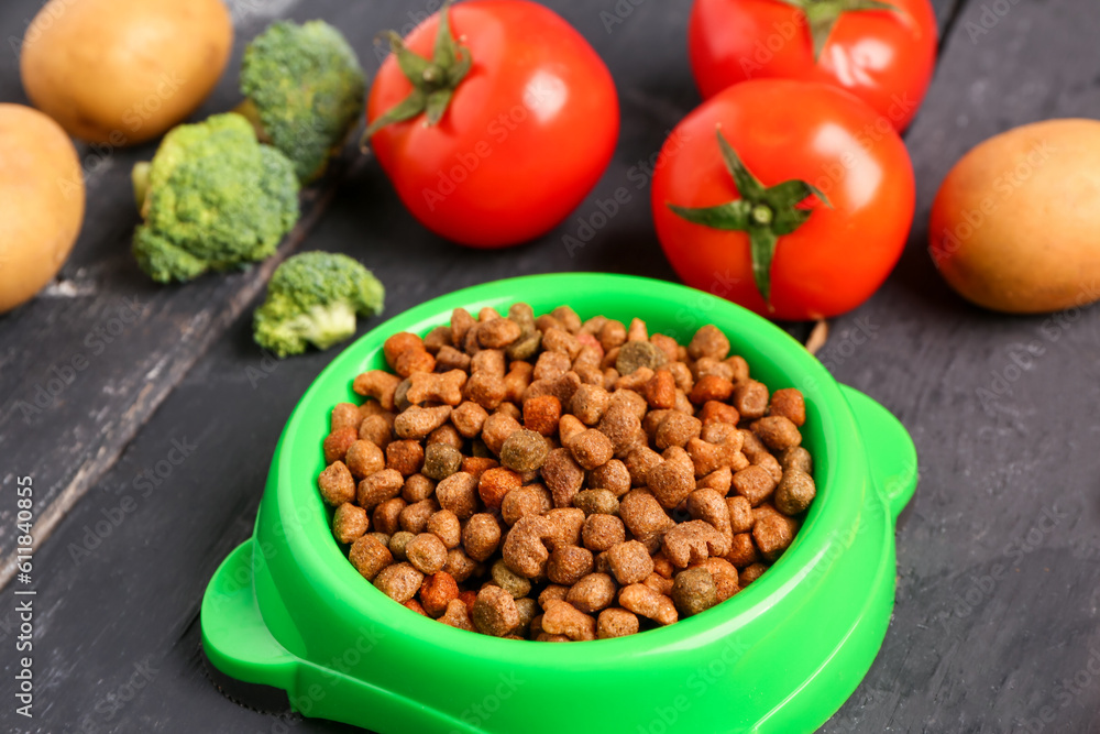 Bowl with dry pet food and natural products on dark wooden background, closeup