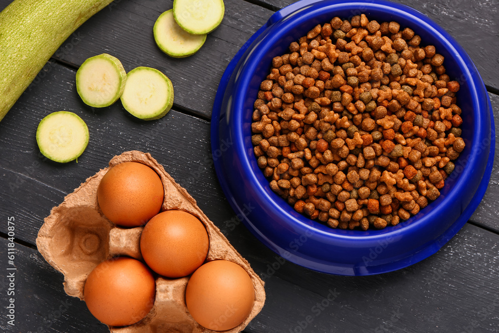 Bowl with dry pet food and natural products on dark wooden background, closeup