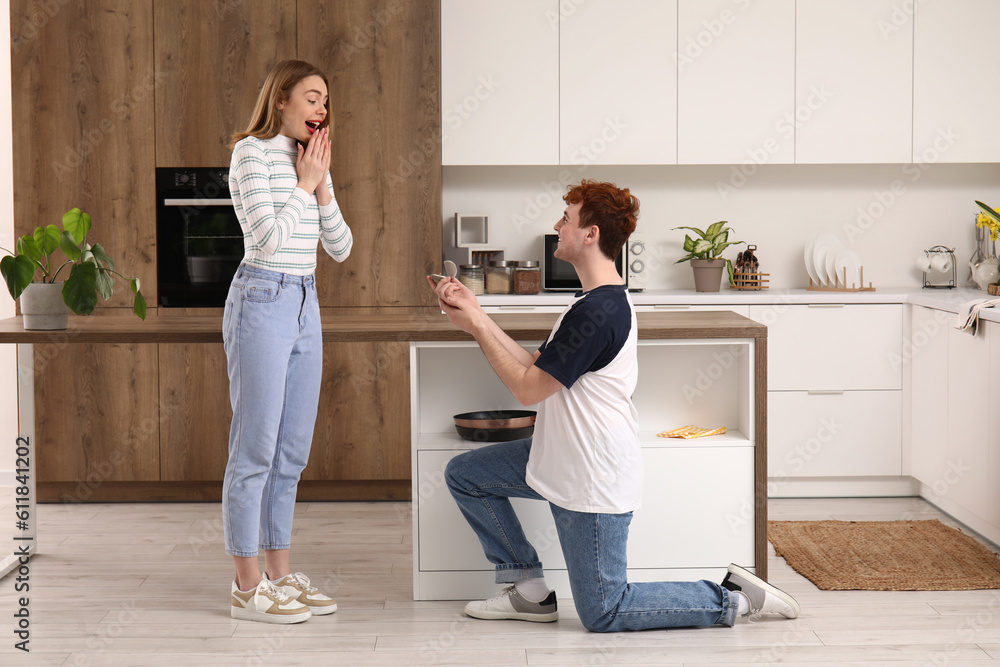 Young man proposing to his happy girlfriend in kitchen