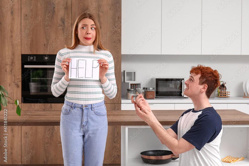 Young man proposing to his girlfriend with word HELP in kitchen