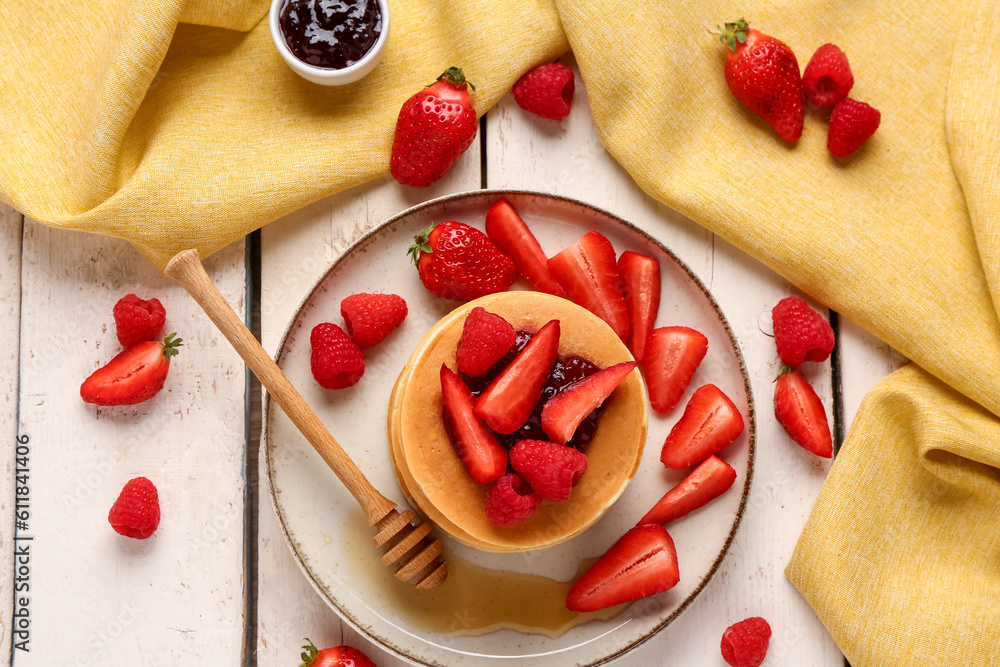 Plate with sweet pancakes, berries and jam on light wooden background