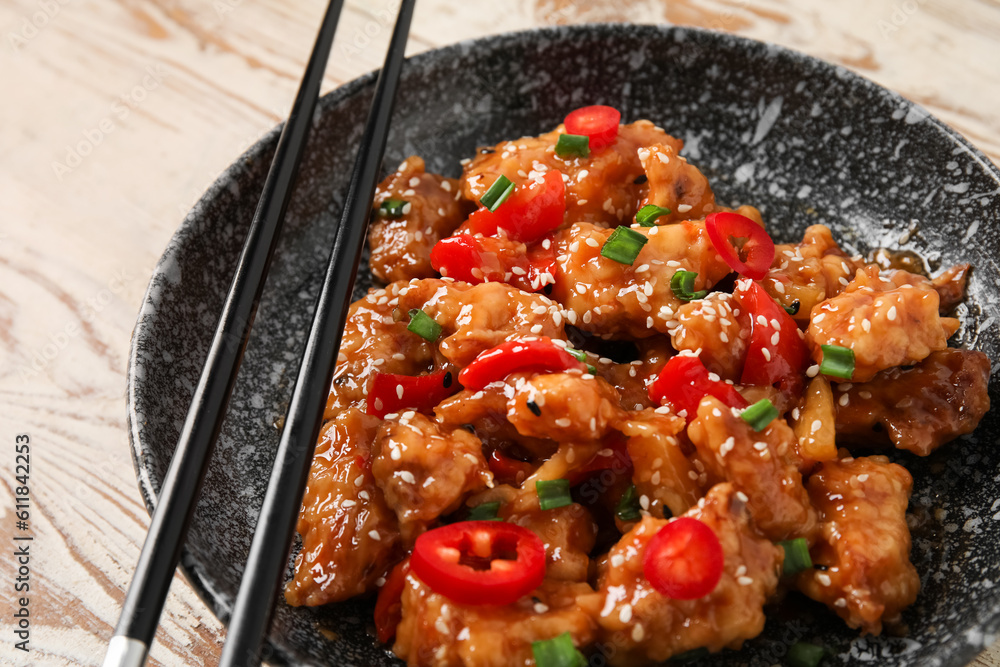 Bowl with tasty sweet and sour chicken on light wooden background, closeup