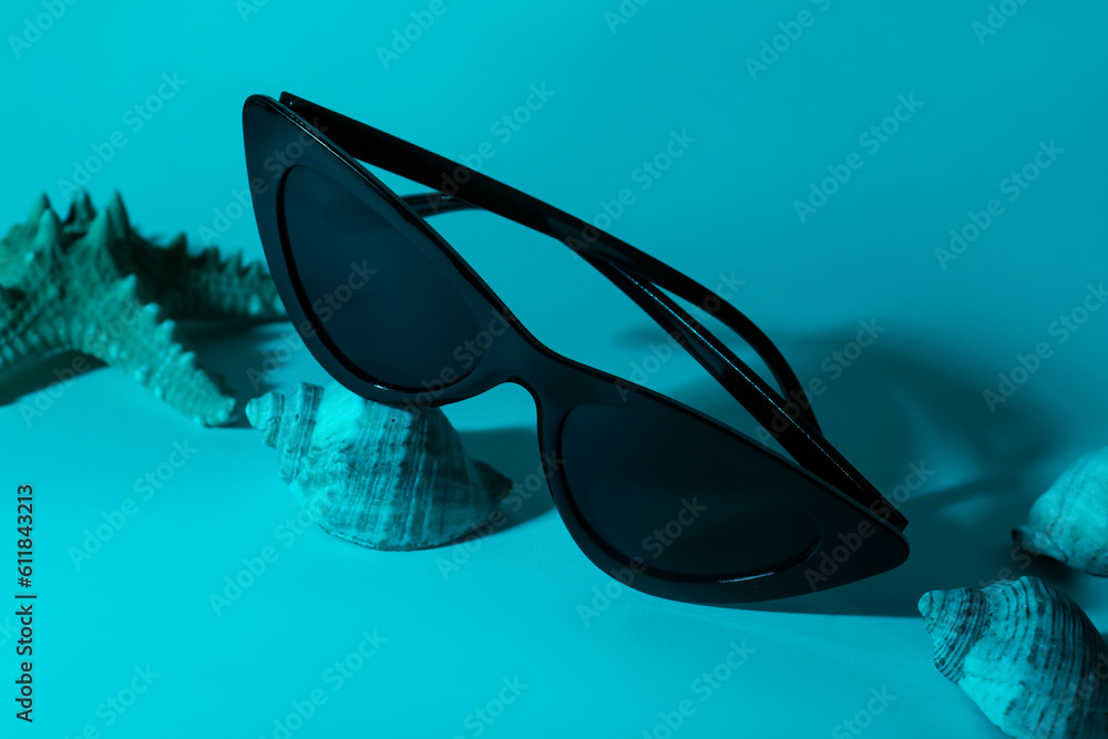 Stylish sunglasses with starfish and shell on blue background