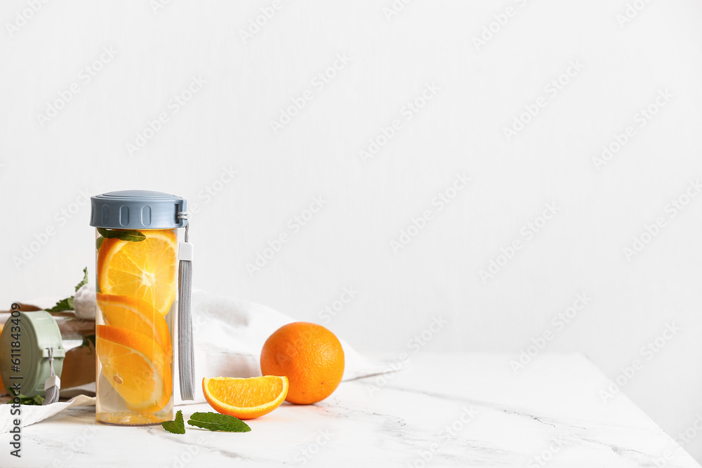 Sports bottles of infused water with orange slices on white table