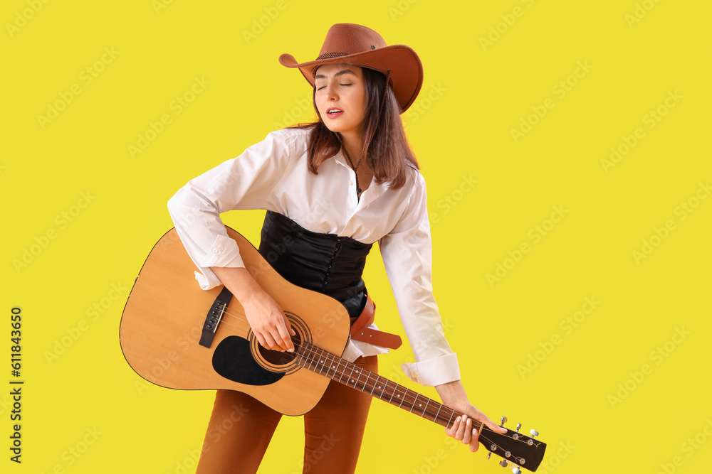 Beautiful cowgirl playing guitar on yellow background