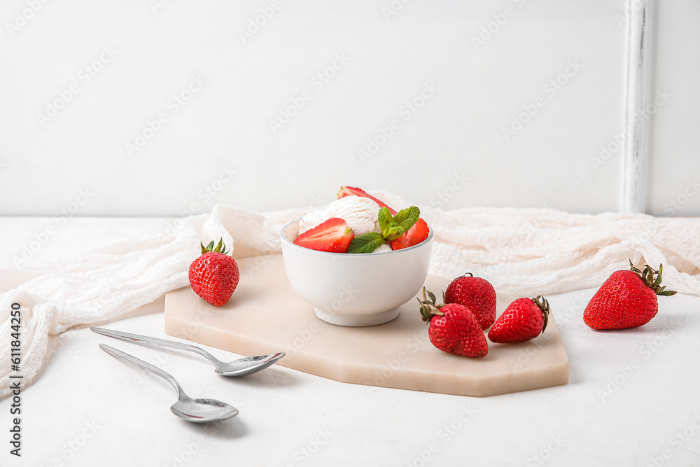 Bowl of vanilla ice cream with strawberries, mint and spoons on white table