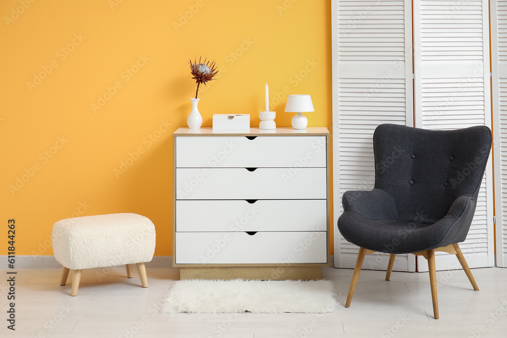 Dark grey armchair with dressing screen, dresser and fluffy rug near orange wall