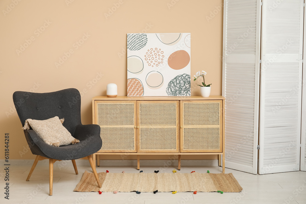 Dark grey armchair with dressing screen, dresser and pillow near beige wall