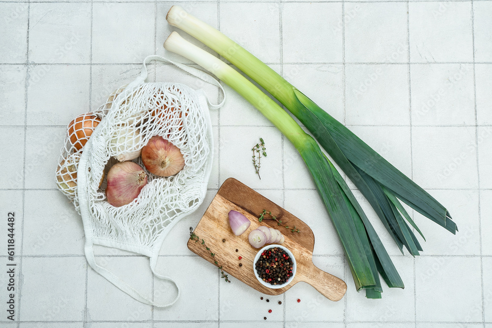 Wooden board and string bag with different kinds of onion on white tile background