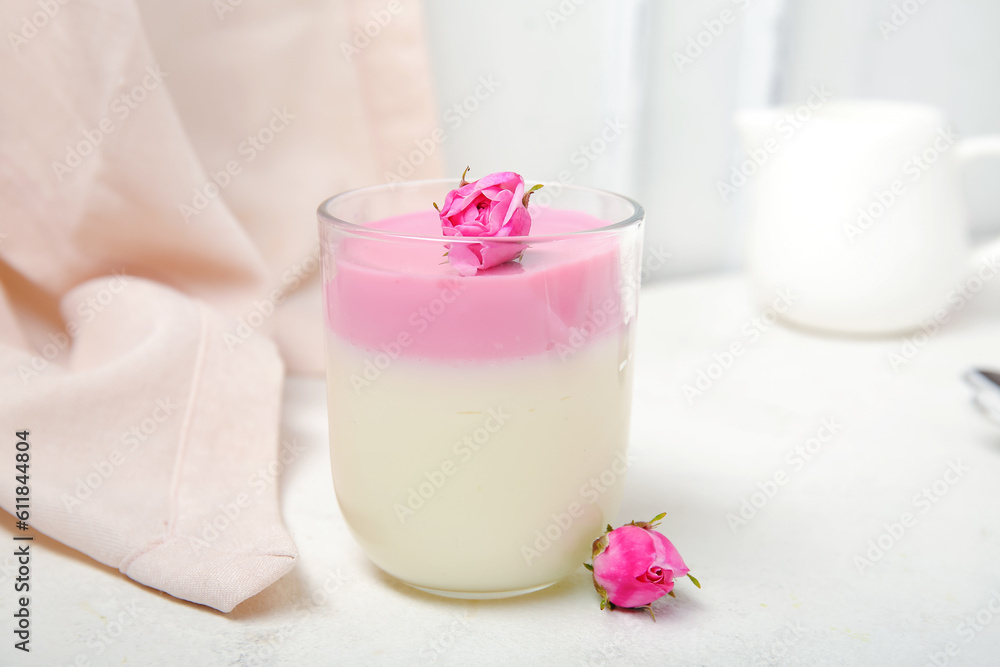 Glass of panna cotta with beautiful pink rose flowers on white table