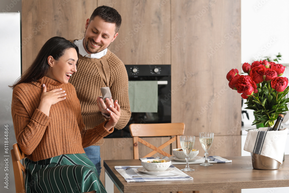 Young man proposing to his happy girlfriend in kitchen