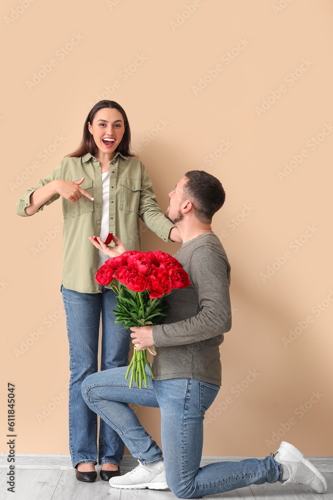 Young man with flowers proposing to his girlfriend near beige wall