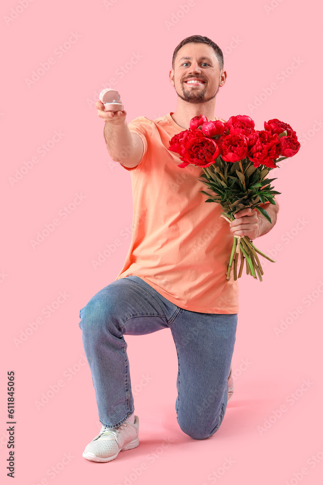 Young man with engagement ring and flowers on pink background