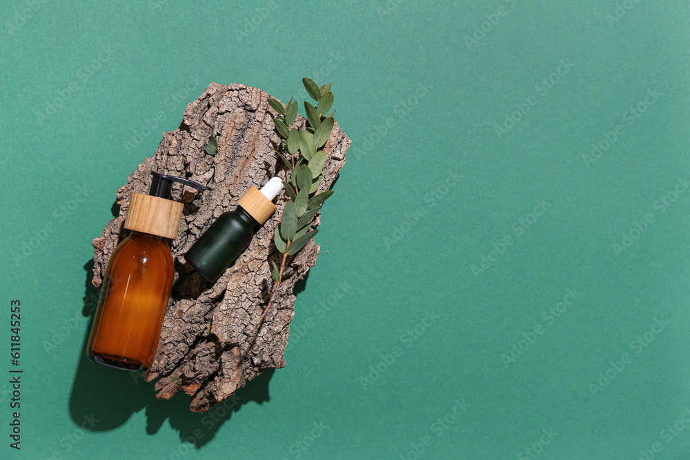 Bottles of cosmetic products, tree bark and eucalyptus branch on color background