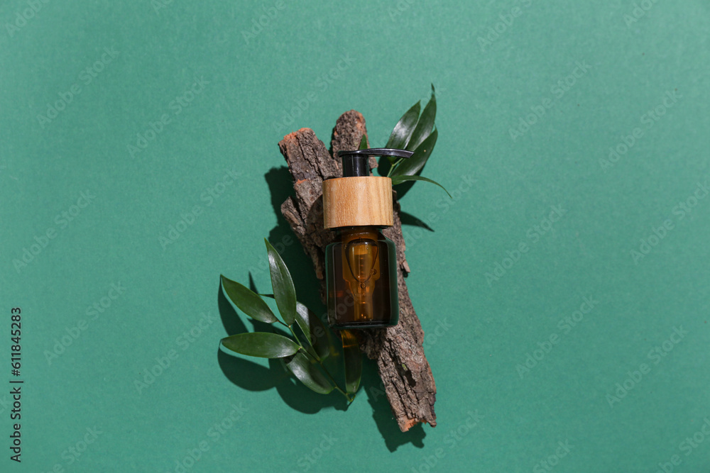 Composition with bottle of cosmetic product, tree bark and plant leaves on green background