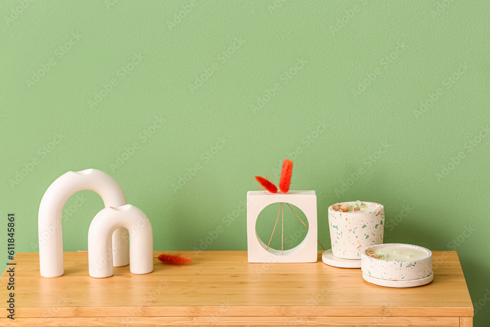 Holders with candles and decor on table near color wall in room