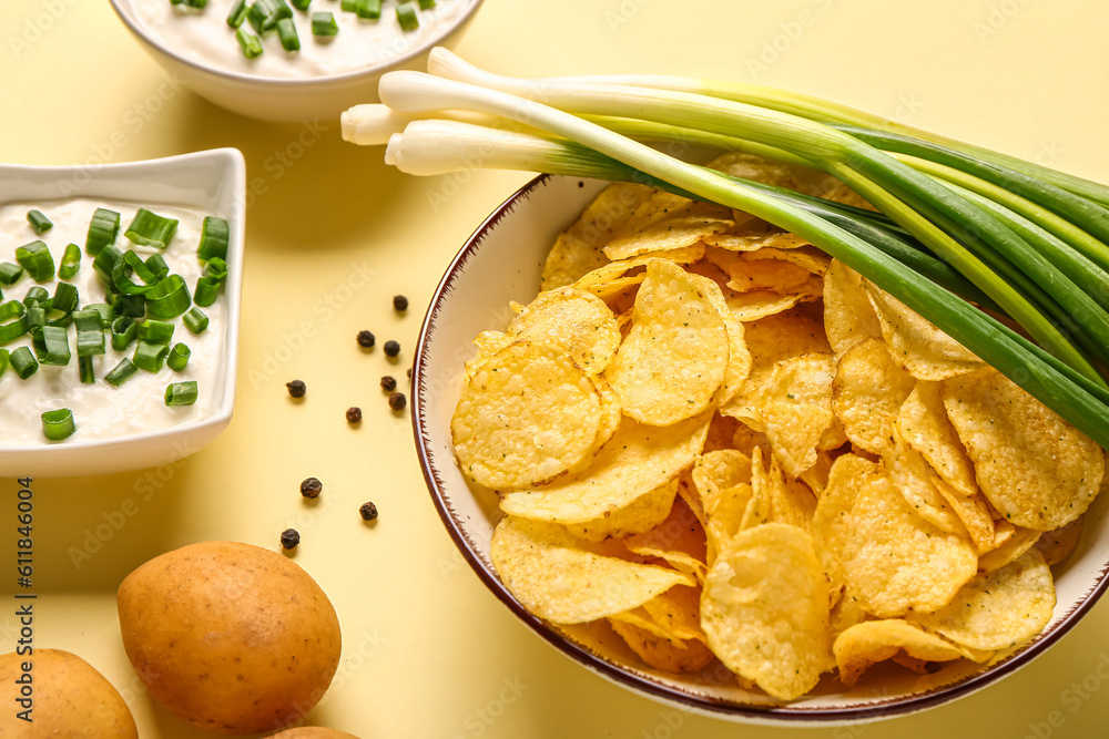 Bowls of tasty sour cream with sliced green onion and potato chips on yellow background