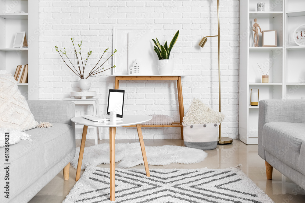 Stylish interior of light living room with modern laptop on table