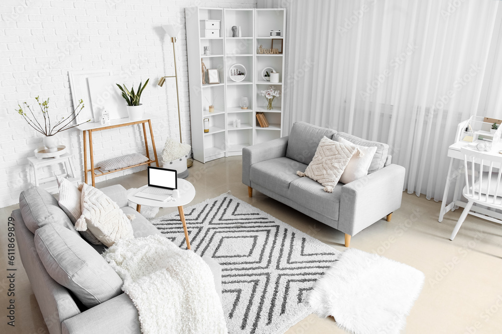 Stylish interior of light living room with sofas and modern laptop on table