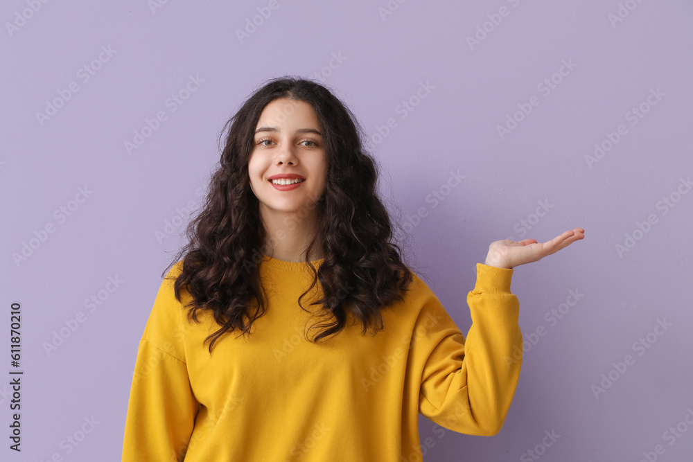 Teenage girl in yellow sweatshirt showing something on lilac background