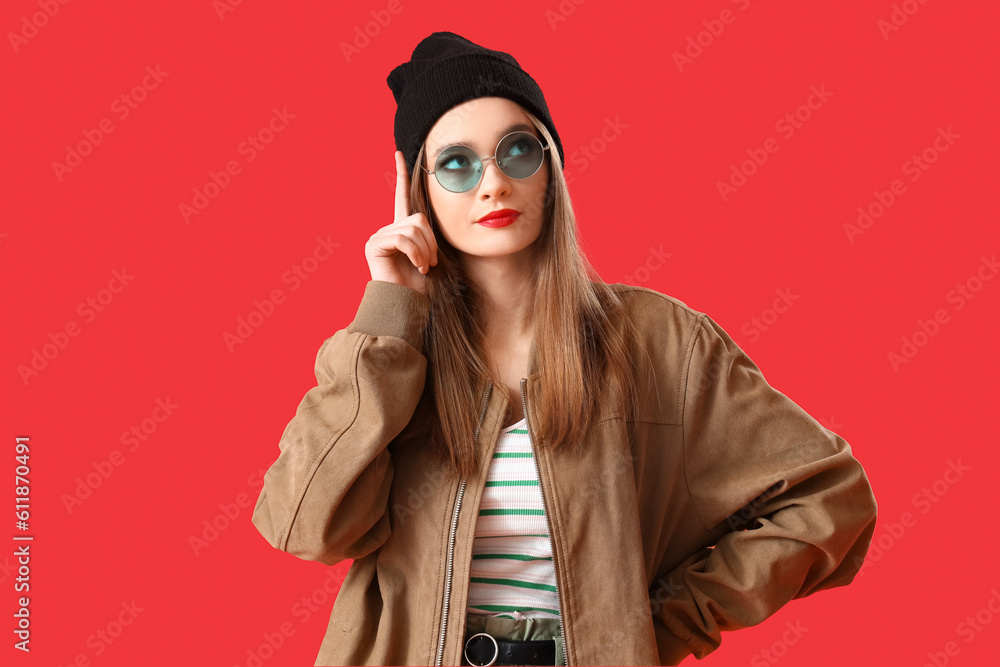 Thoughtful young woman in sunglasses on red background