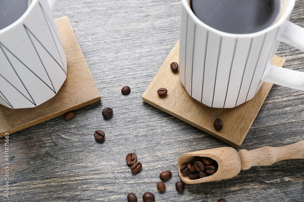 Drink coasters with cups of coffee and beans on wooden table