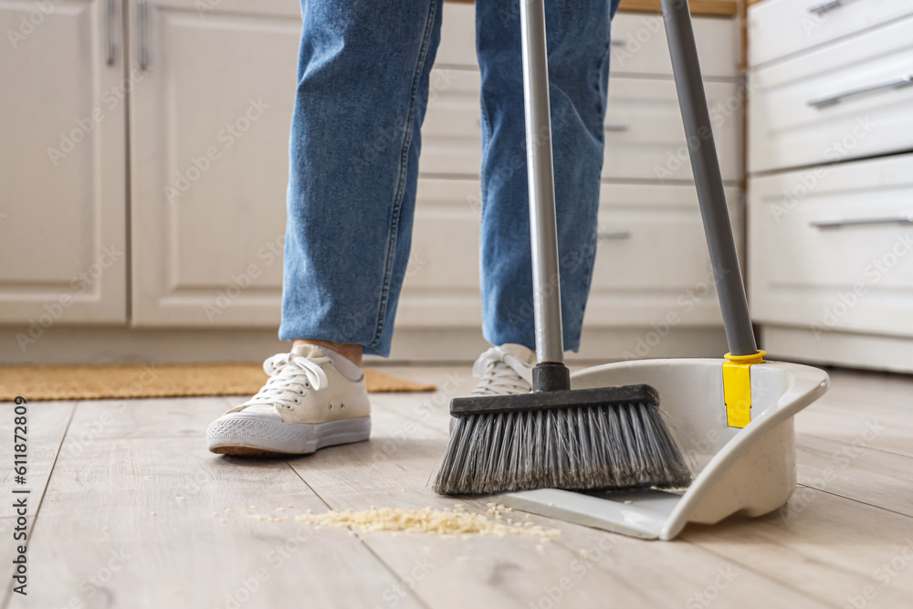 Housewife cleaning floor with broom and dustpan in kitchen, closeup