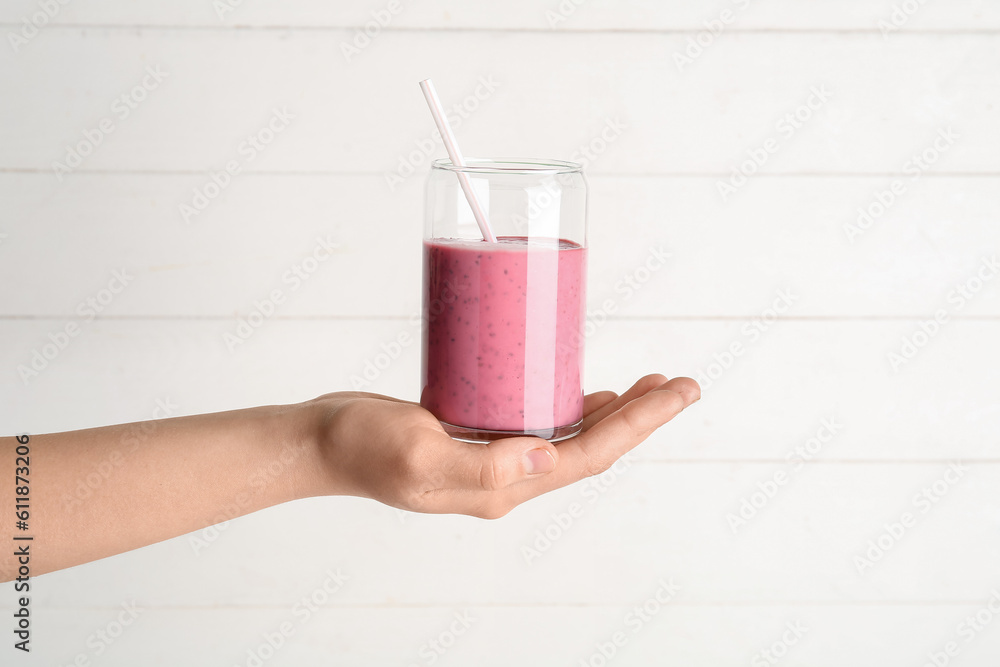 Female hand with glass of pink smoothie on white background