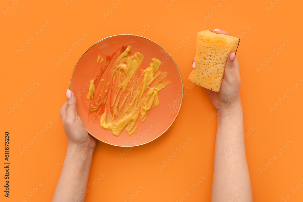 Female hands washing dirty plate with sponge on orange background