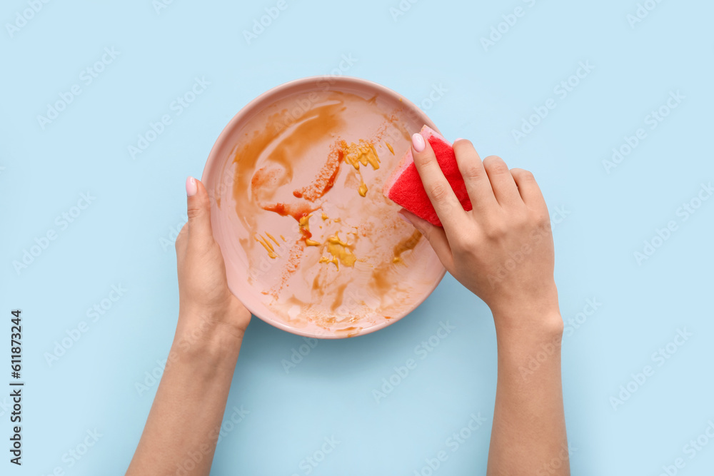 Female hands washing dirty plate with sponge on blue background